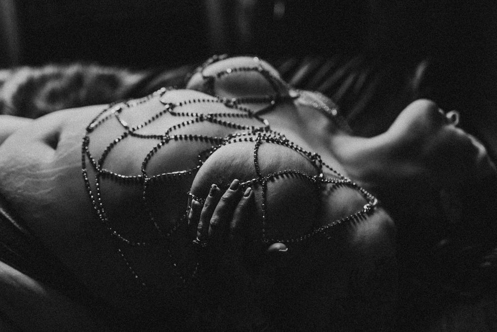 Black and white artistic nude study with intricate body jewelry creating geometric patterns.