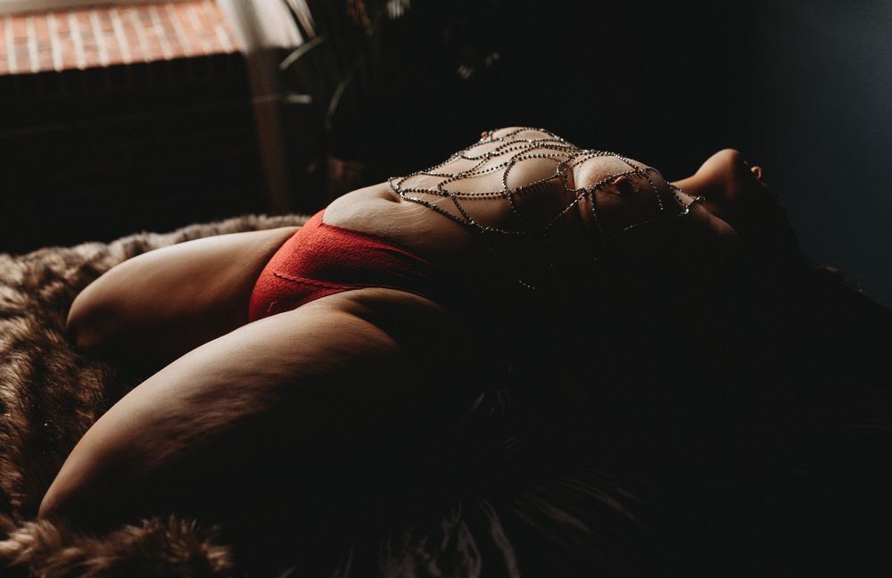Artistic boudoir shot in red lingerie with soft lighting and textured backdrop.