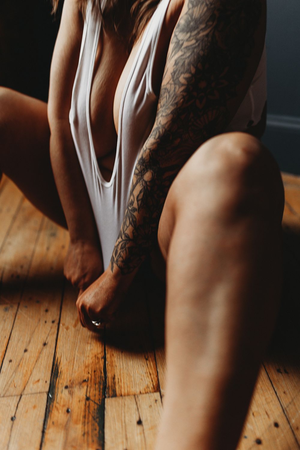 Close-up shot of tattooed arm and white fabric against wooden floorboards in natural light.