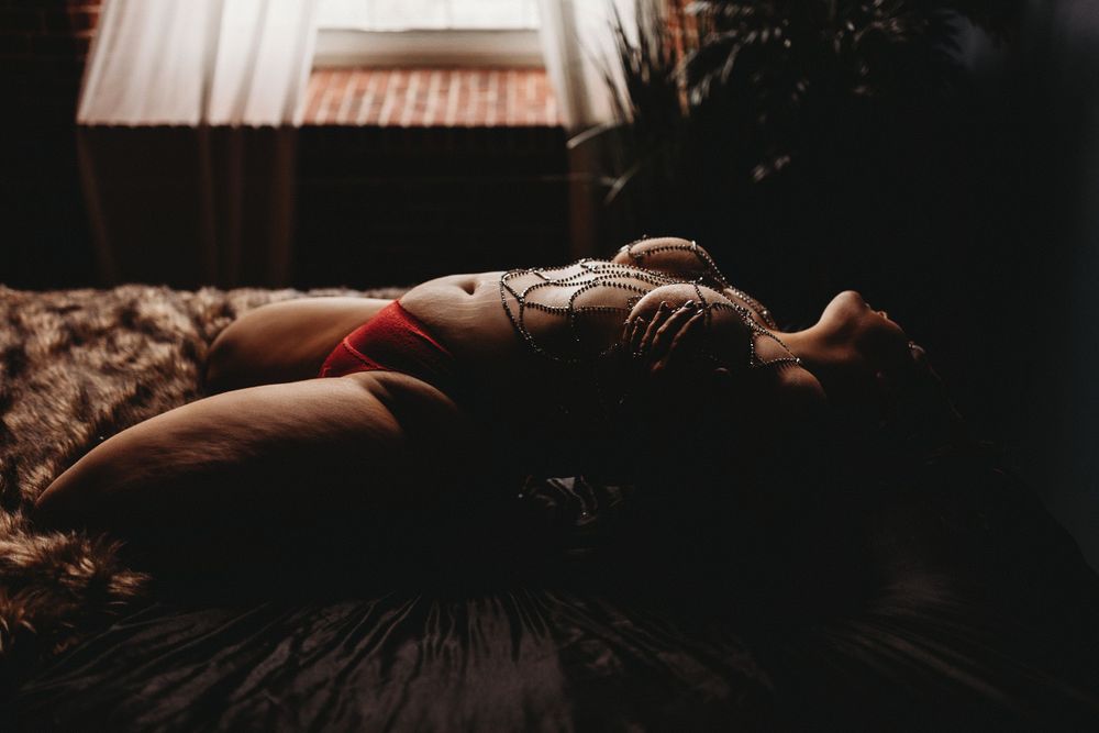 Sensual portrait with ornate body jewelry in warm natural window light.