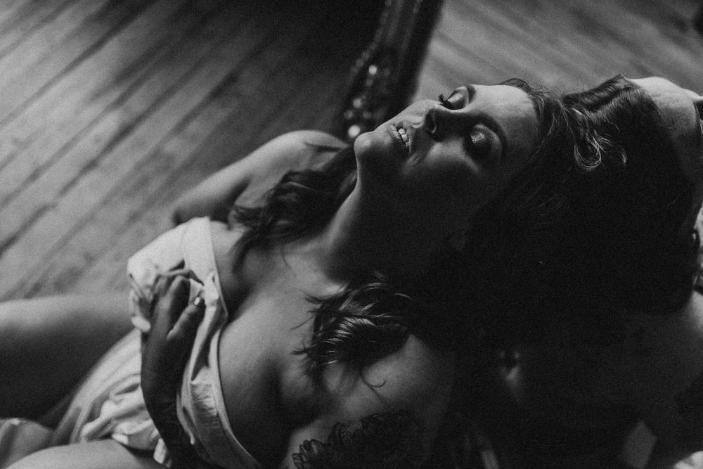 Intimate black and white photograph showing two people in tender embrace on wooden floor.