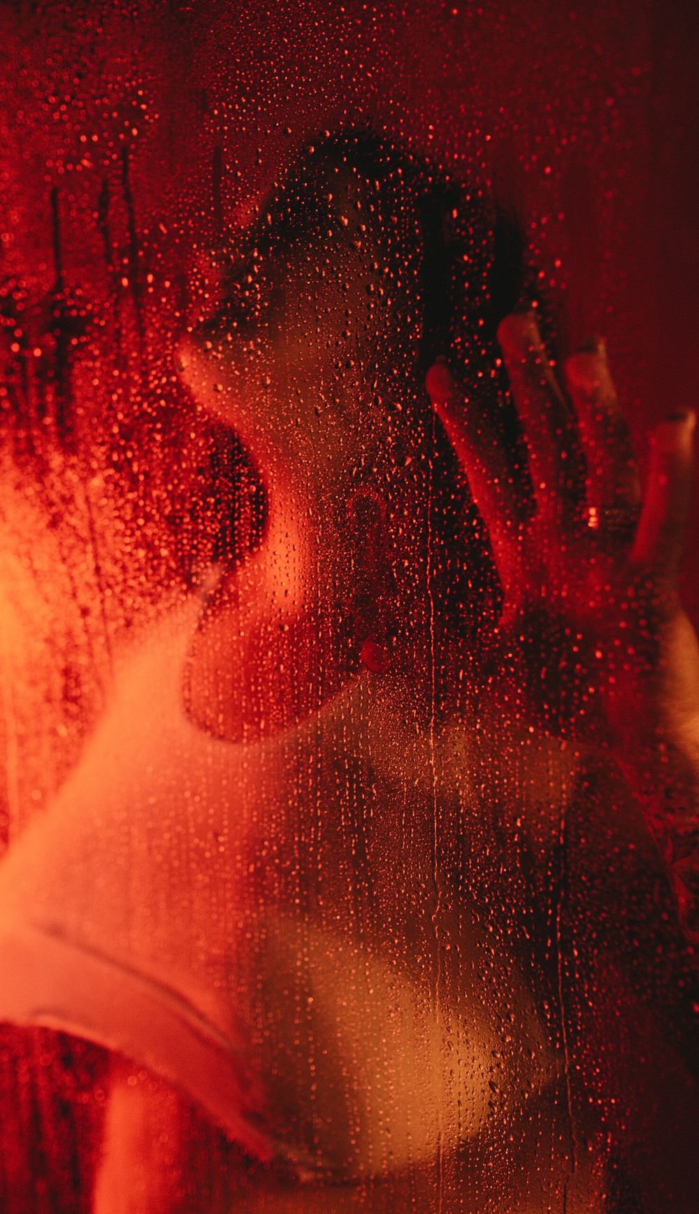 Silhouette behind wet glass with red lighting creating moody atmosphere.