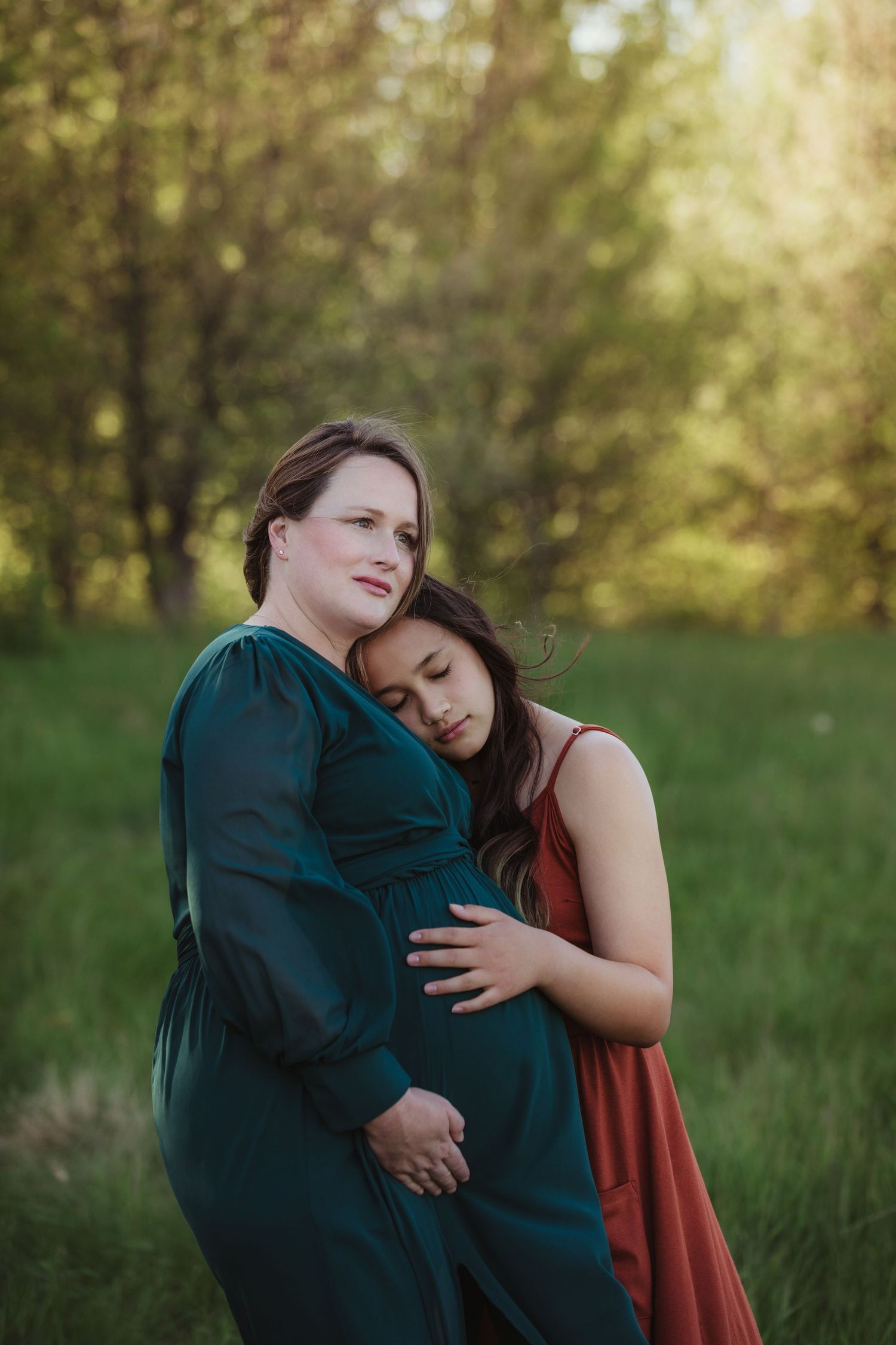 Two people sharing an intimate embrace in a green outdoor setting during golden hour.