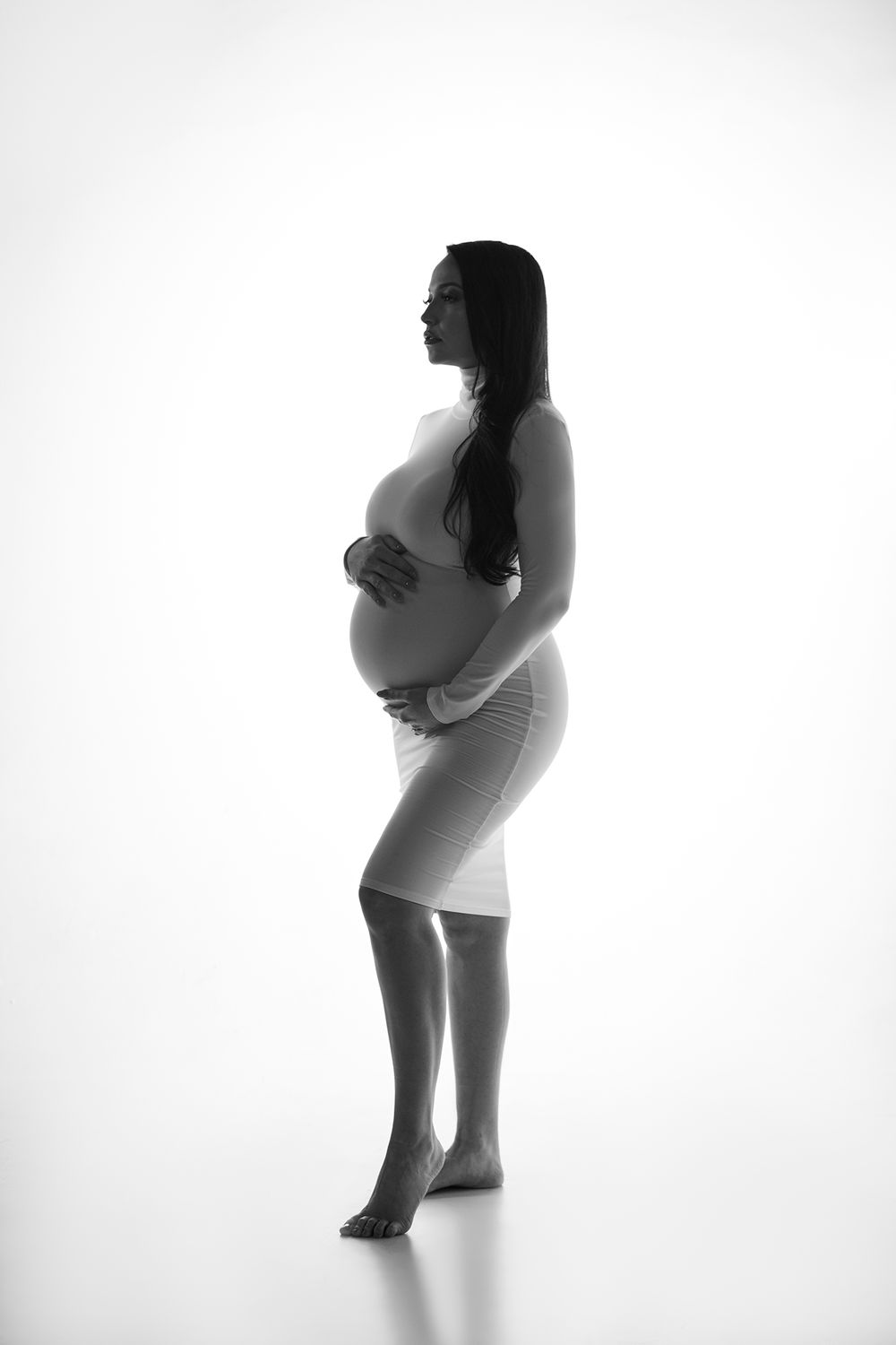 Black and white silhouette of an expectant mother in a form-fitting dress standing against a light background.