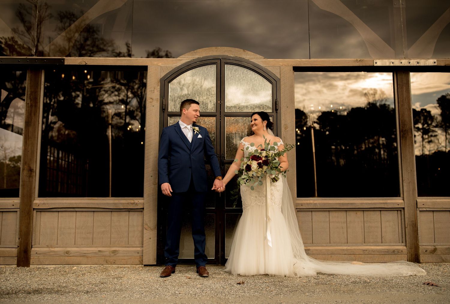 A couple poses together against an arched window backdrop during their rustic outdoor wedding.