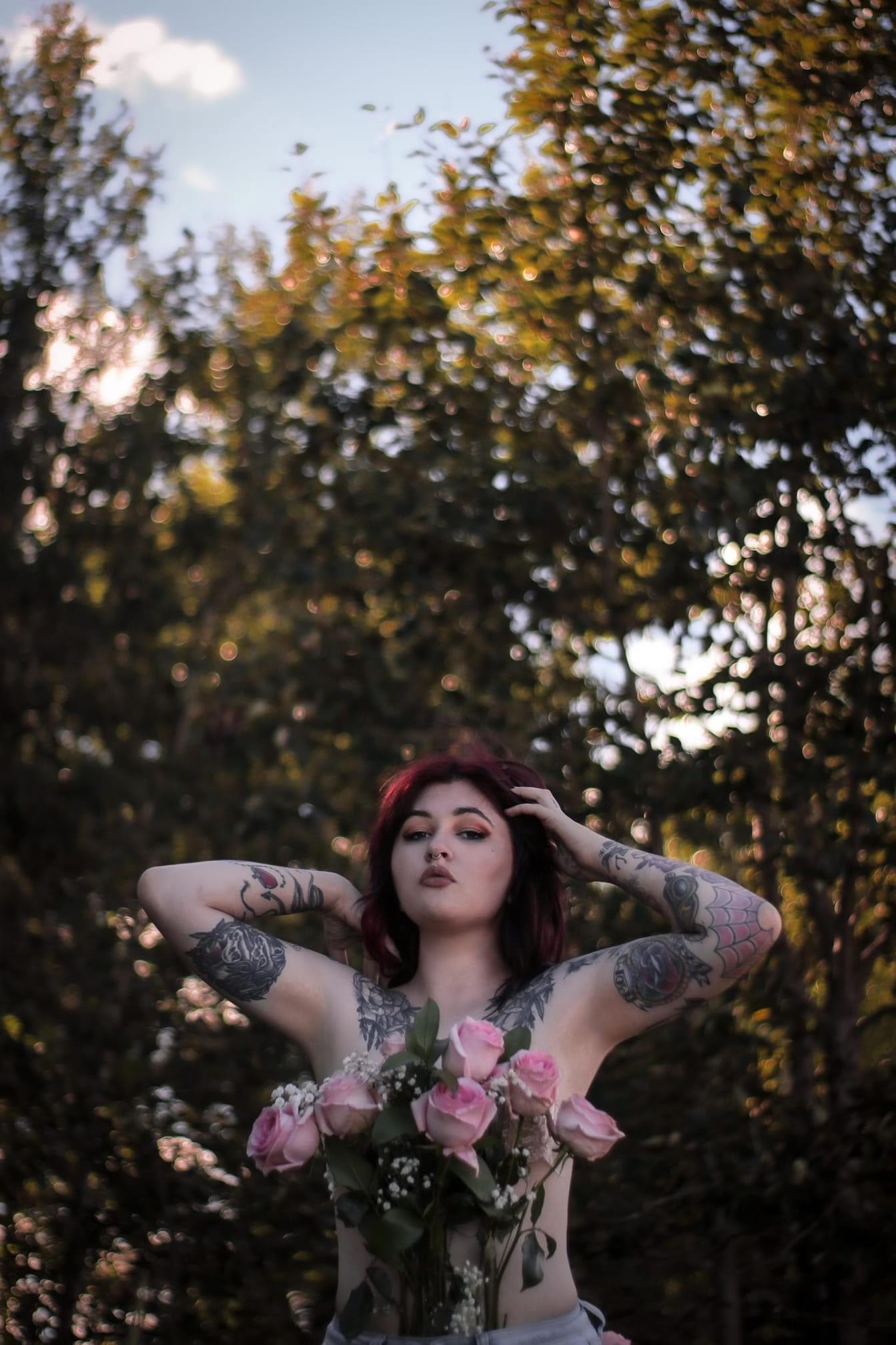 tattooed shirtless woman covering chest with bouquet