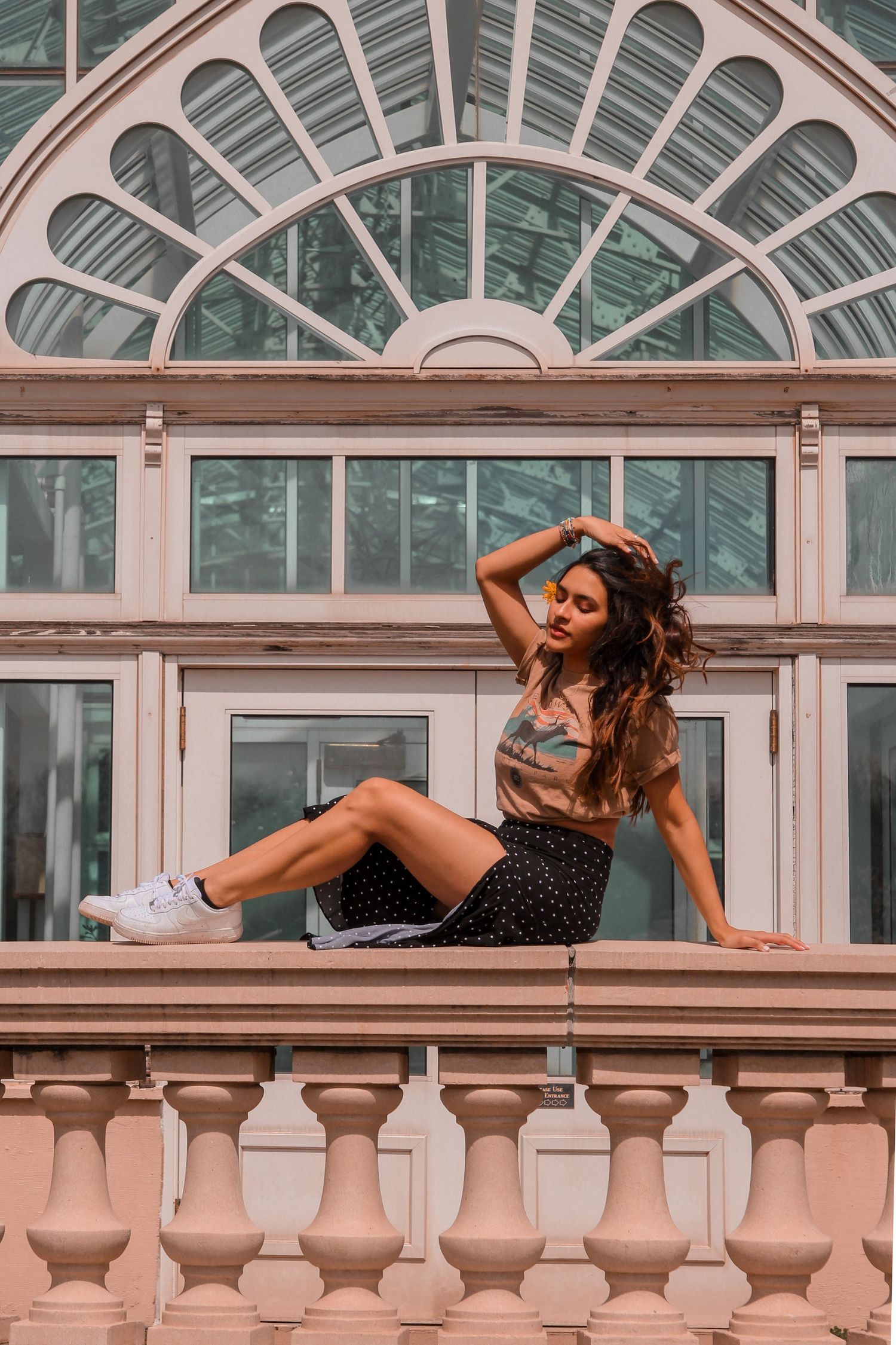 woman wearing 90's fashion posing in front of a massive greenhouse