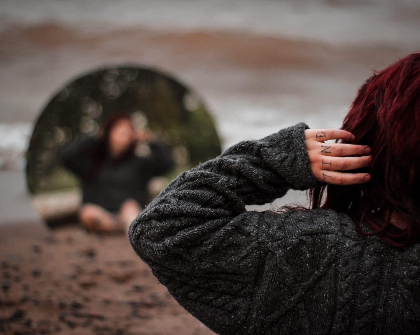 tattooed woman on a moody beach with mirror prop