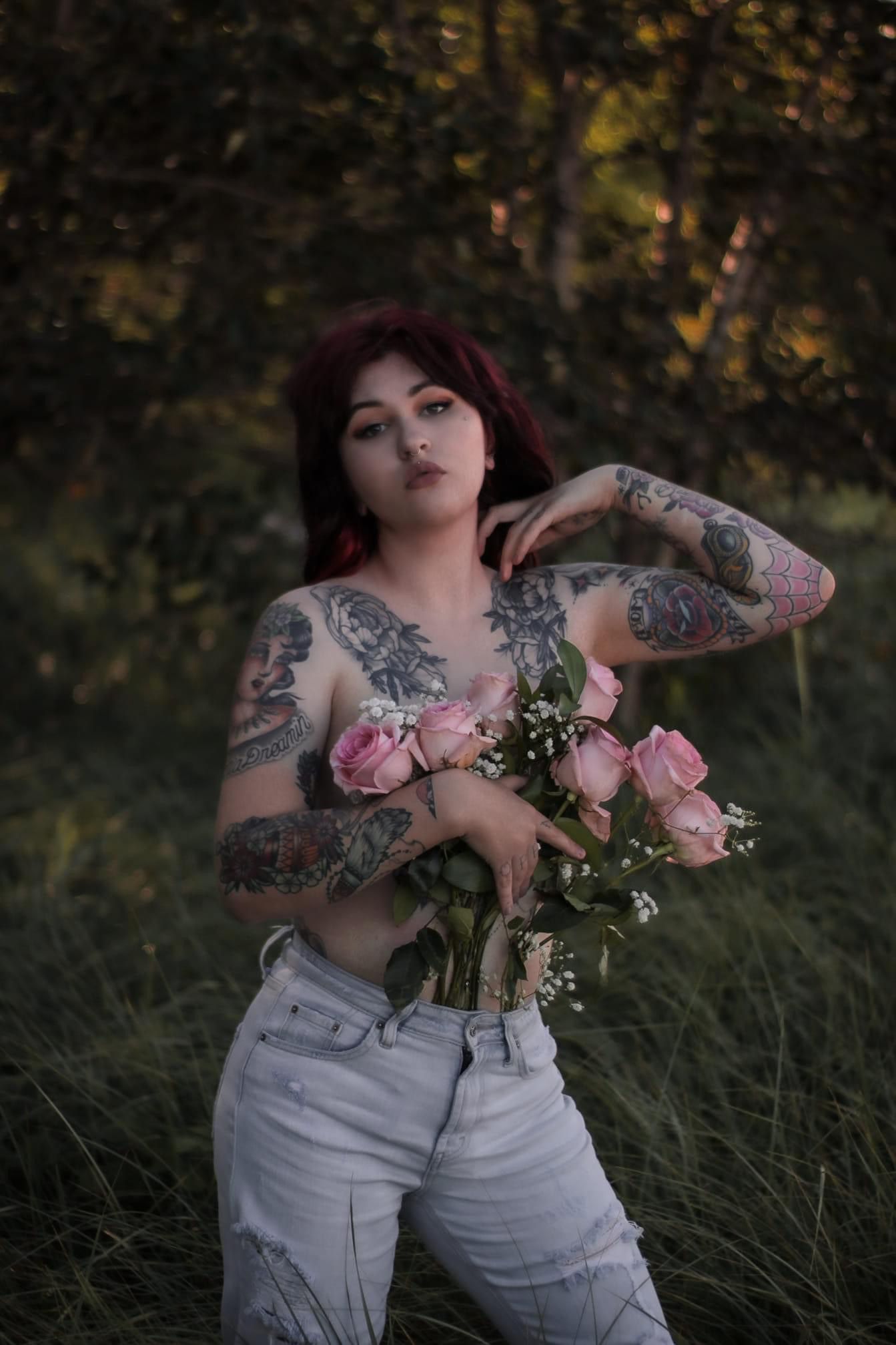 tattooed shirtless woman covering chest with bouquet