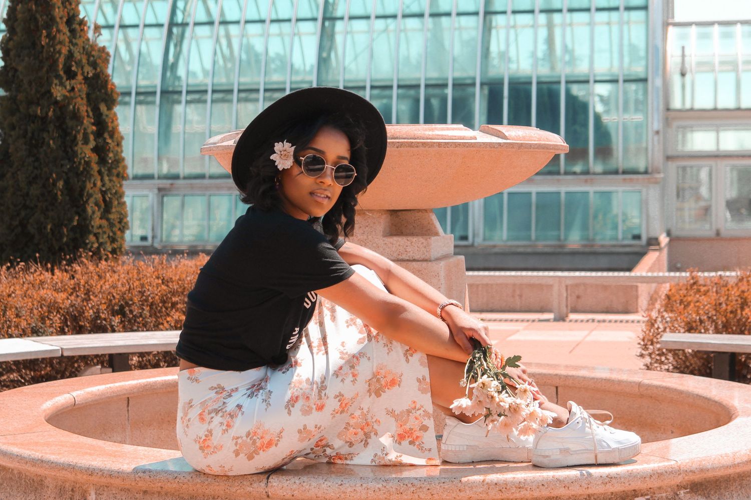 woman wearing 90's fashion posing in front of a massive greenhouse