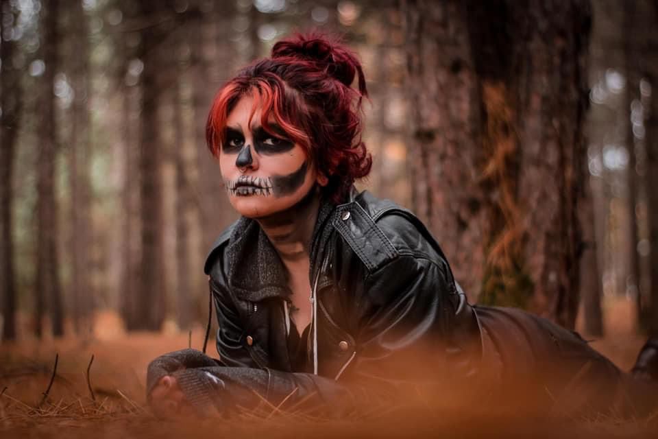 Woman with skull face paint posing in a moody spooky forest