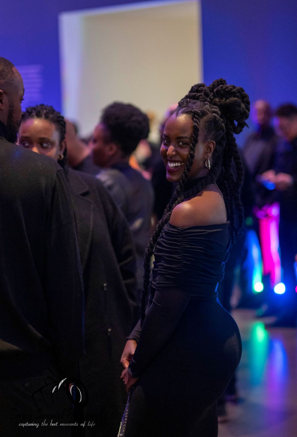People dancing and socializing at a dimly lit event with blue and purple lighting effects in the background.