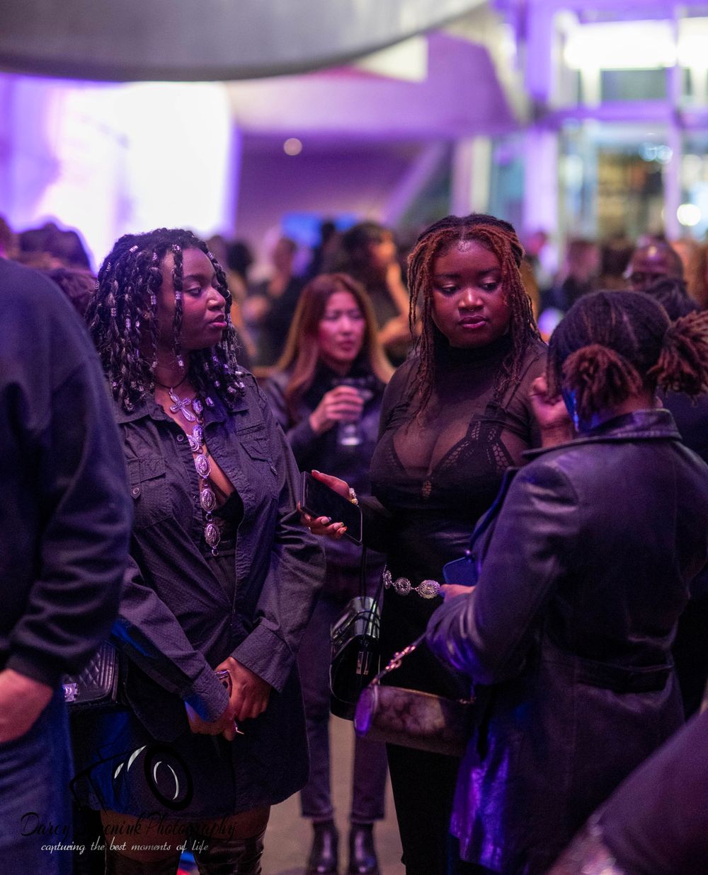 A group of people dancing and socializing at a dimly lit nightclub or party venue with purple lighting.