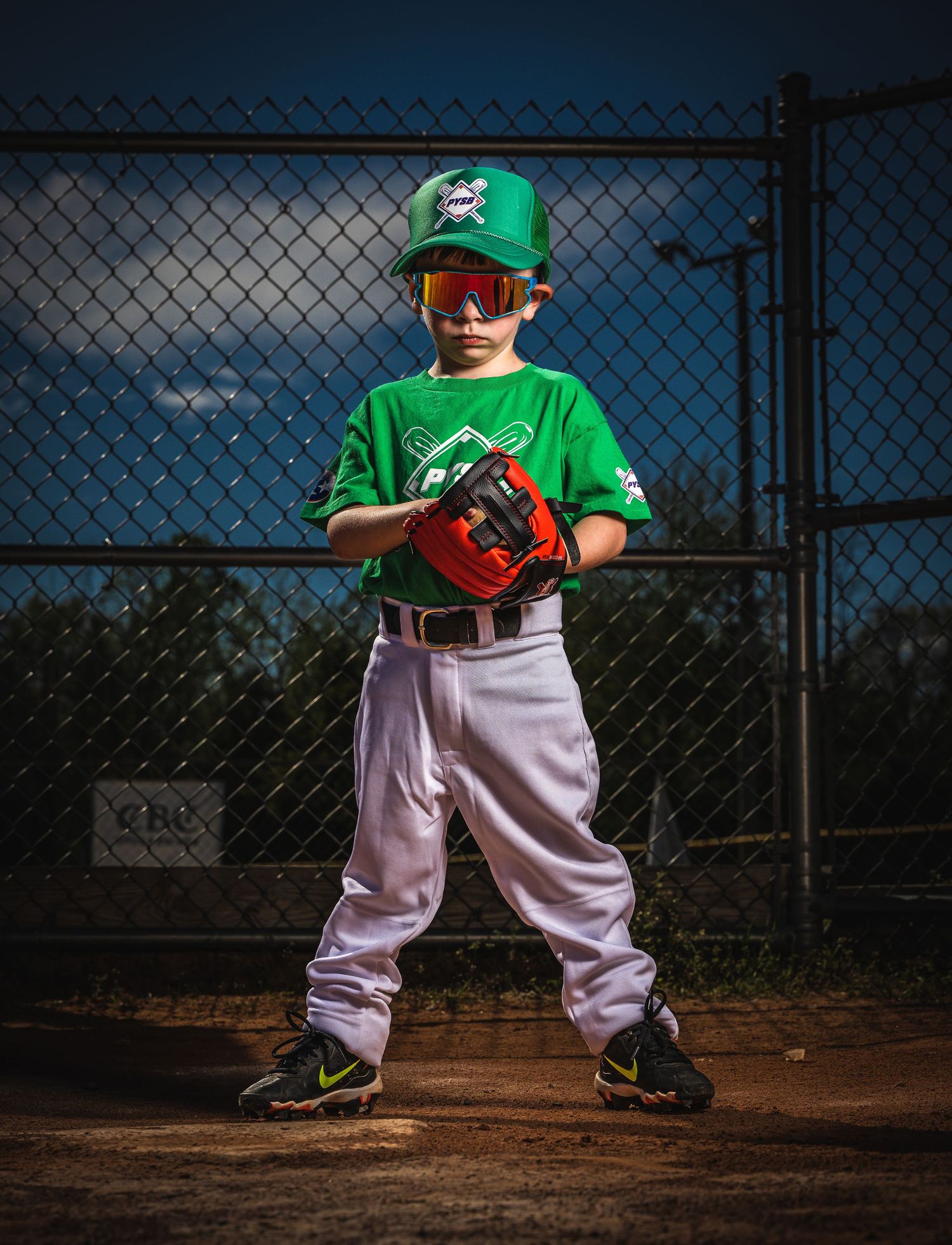 A youth baseball player in green uniform stands ready on the baseball field.