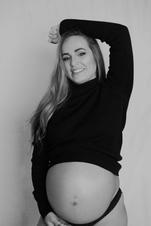 Black and white maternity photo showing a woman in a dark sweater posing with her pregnant belly.