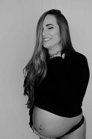Black and white maternity photo of expectant mother in dark sweater showing joyful expression.