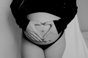 Black and white photo of hands forming heart shape on pregnant belly.