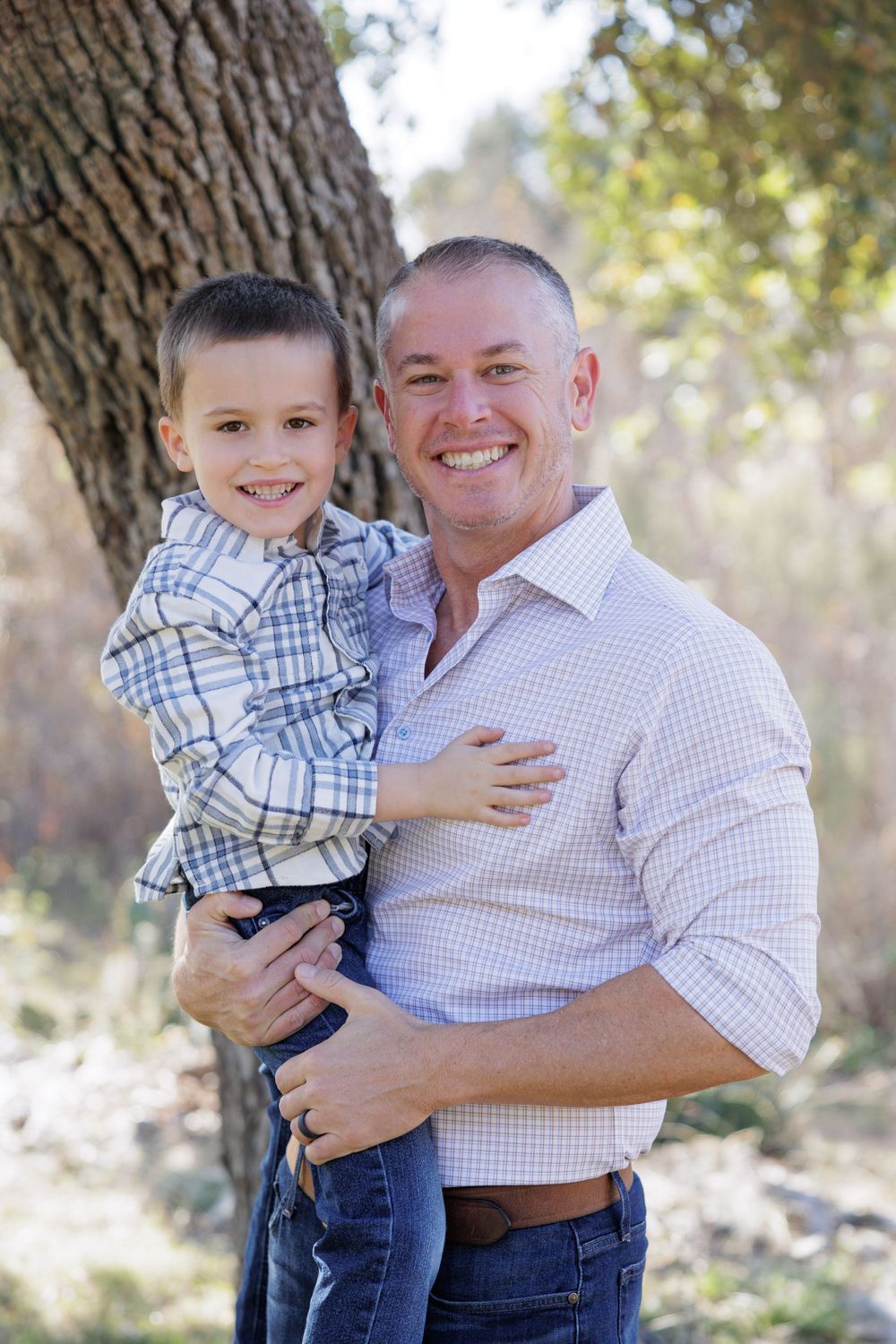 A happy outdoor portrait in natural lighting shows a parent and child wearing coordinating plaid shirts.