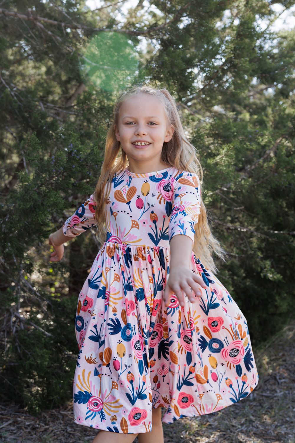 A young girl in a floral dress twirls outdoors against a natural backdrop.