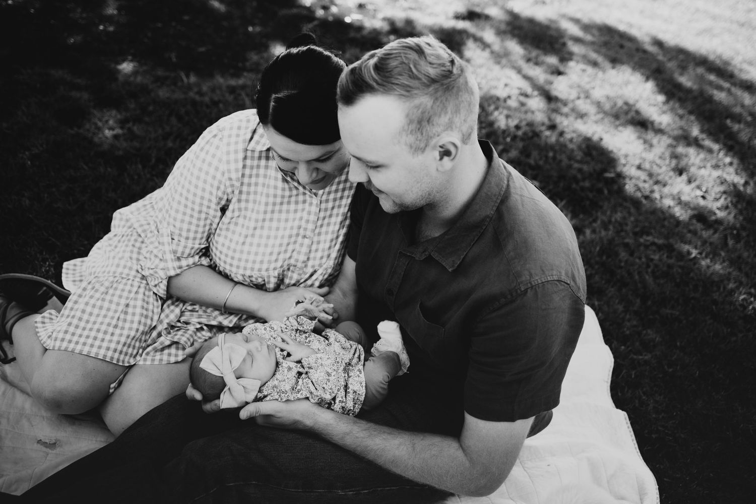 Black and white image of parents lovingly gazing at their newborn baby on a blanket.