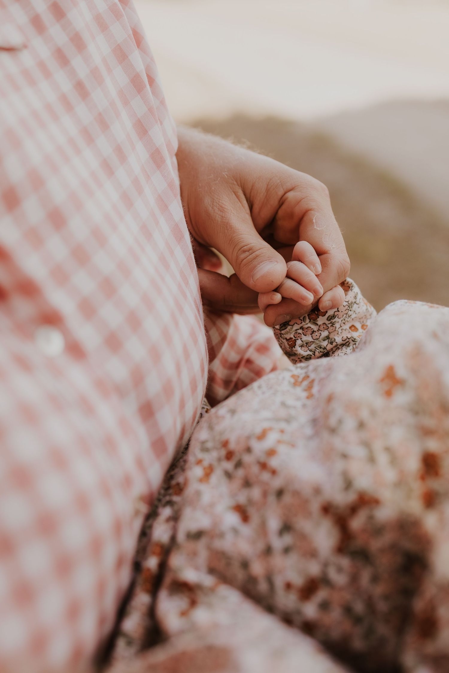 Tender close-up of a newborn babys tiny hand grasping a parents finger outdoors.