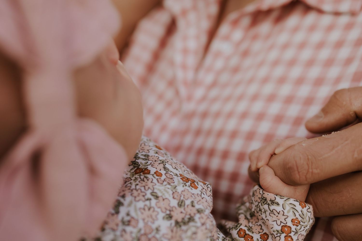 Close-up of a newborn baby girl holding her fathers finger in soft natural light.