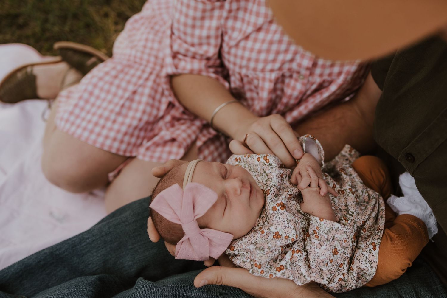 Sleeping newborn baby girl in floral outfit with pink bow headband lying on a blanket.