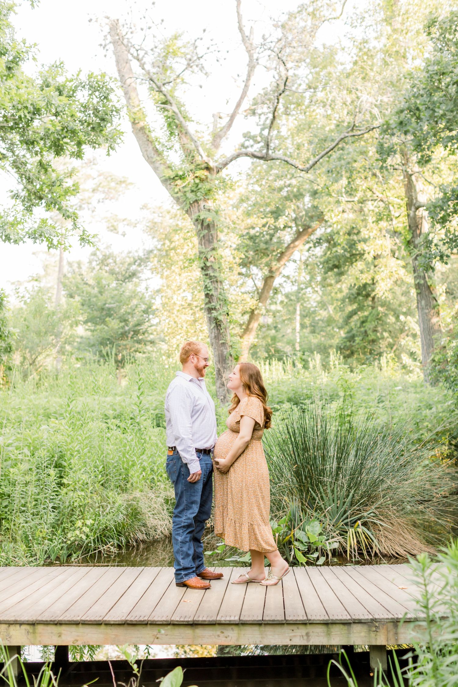 A couple stands on wooden deck surrounded by verdant summer foliage.
