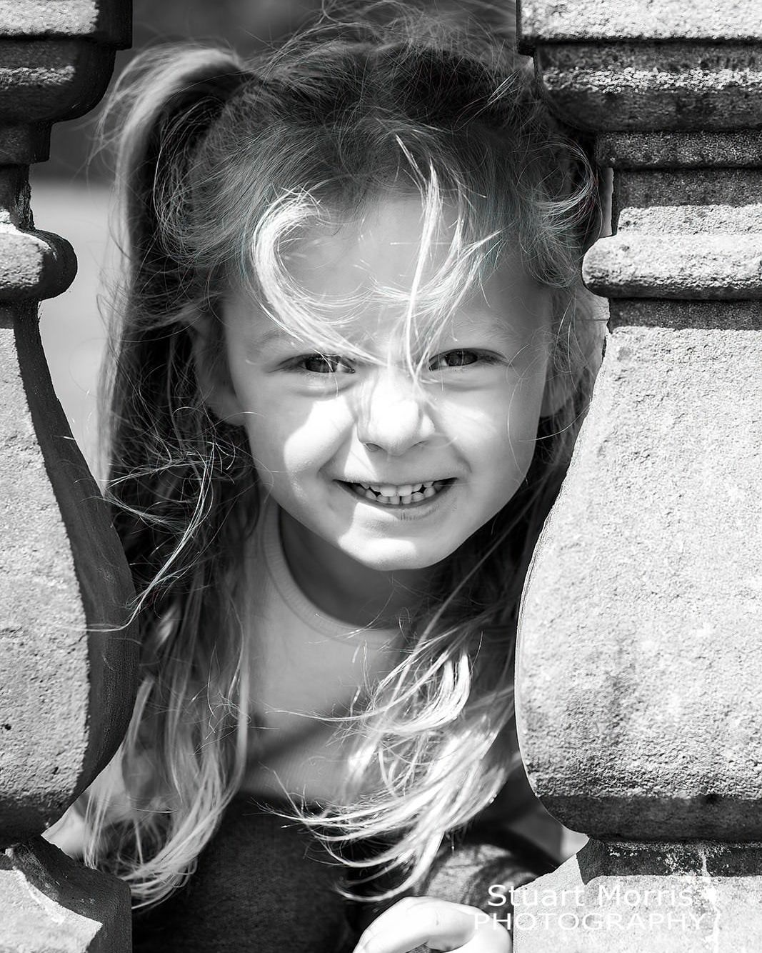 young girl peeps through the stone balustrade at Walton hall garden. mini outdoor photo session warrington