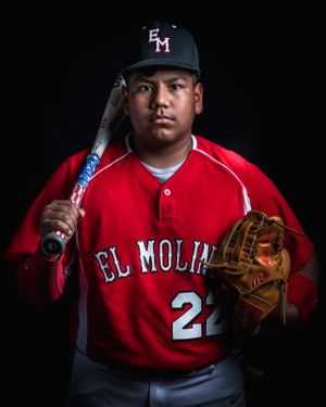 Baseball player in El Molino uniform number 21 poses with bat and glove against black background.