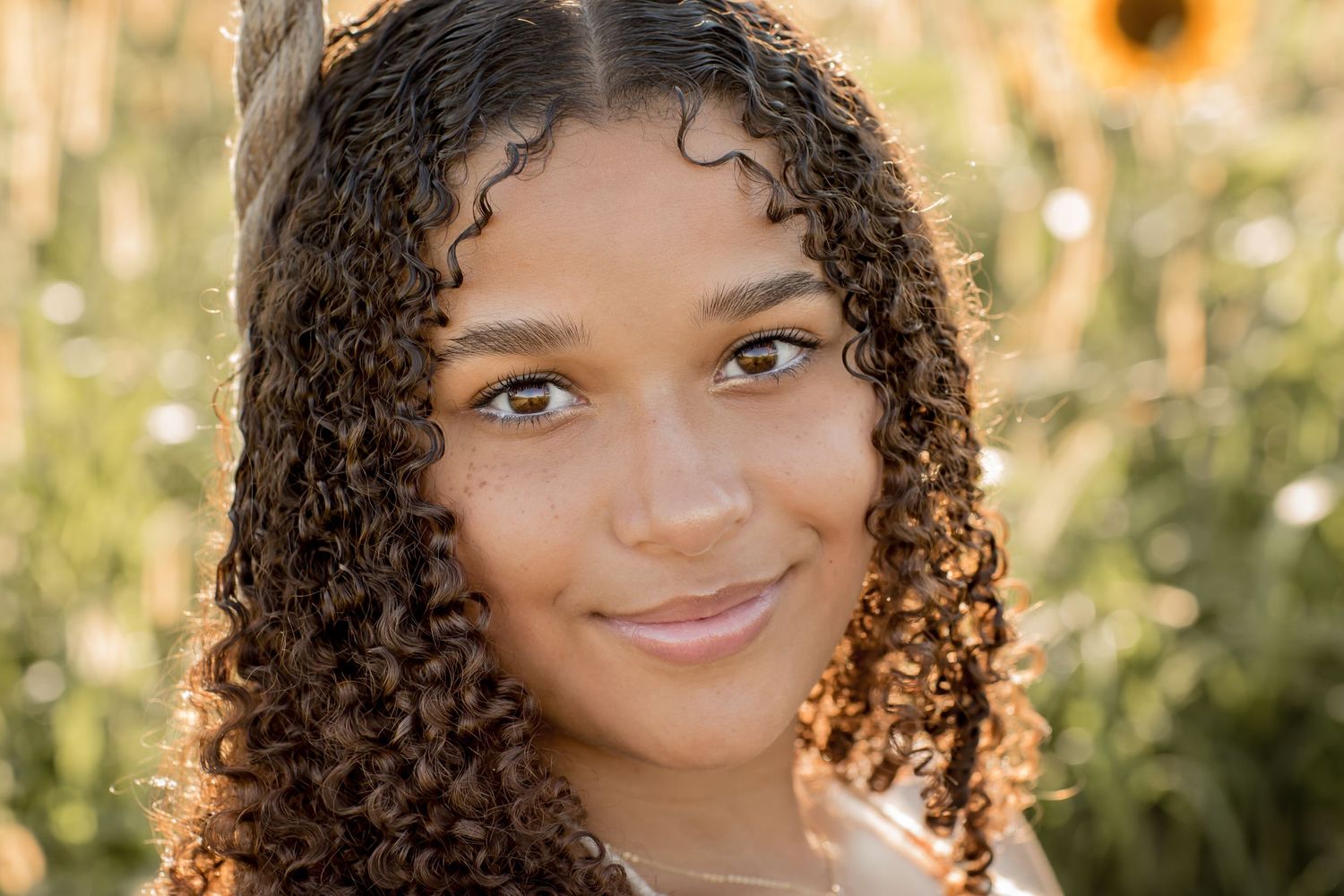 Close-up portrait of young woman with curly hair near sunflowers outdoors.