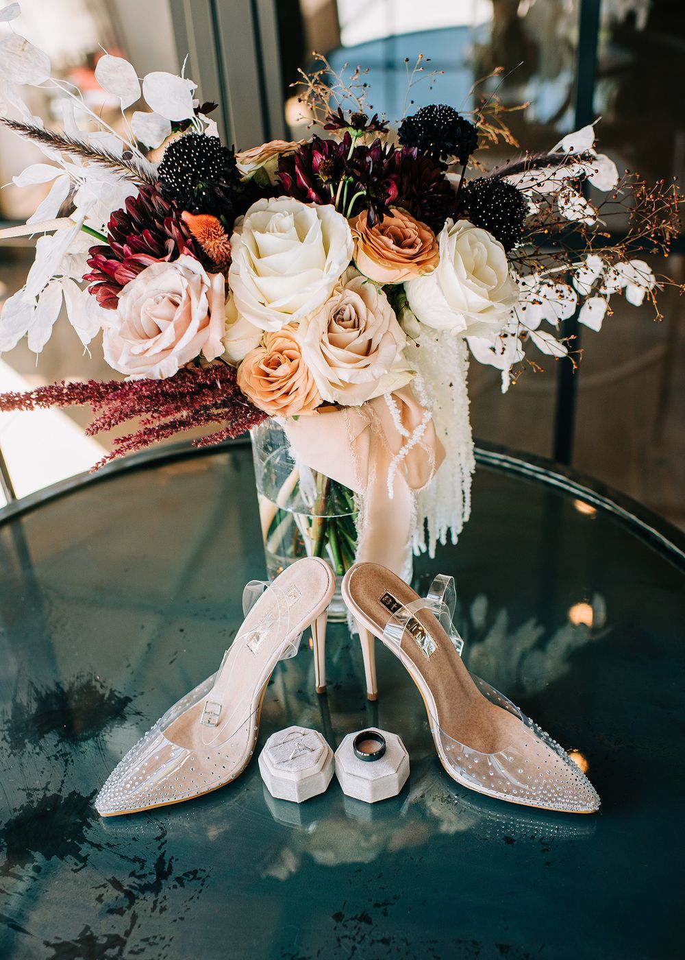 Bridal shoes and wedding rings displayed with romantic pastel floral arrangement.