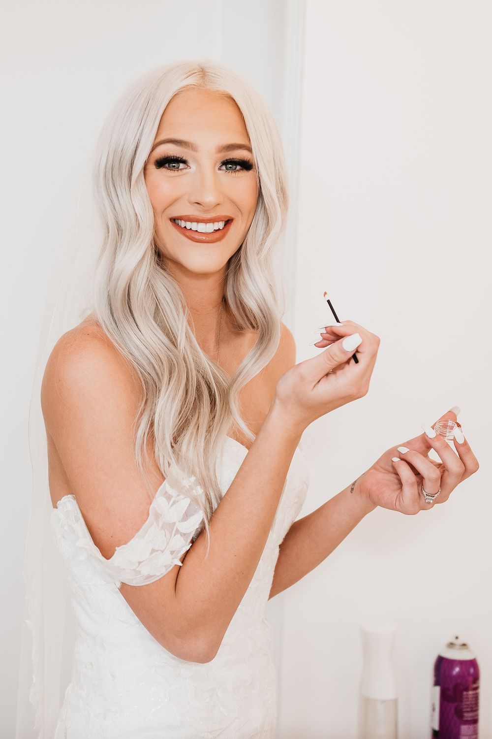 Bride getting ready with makeup in a white strapless dress.