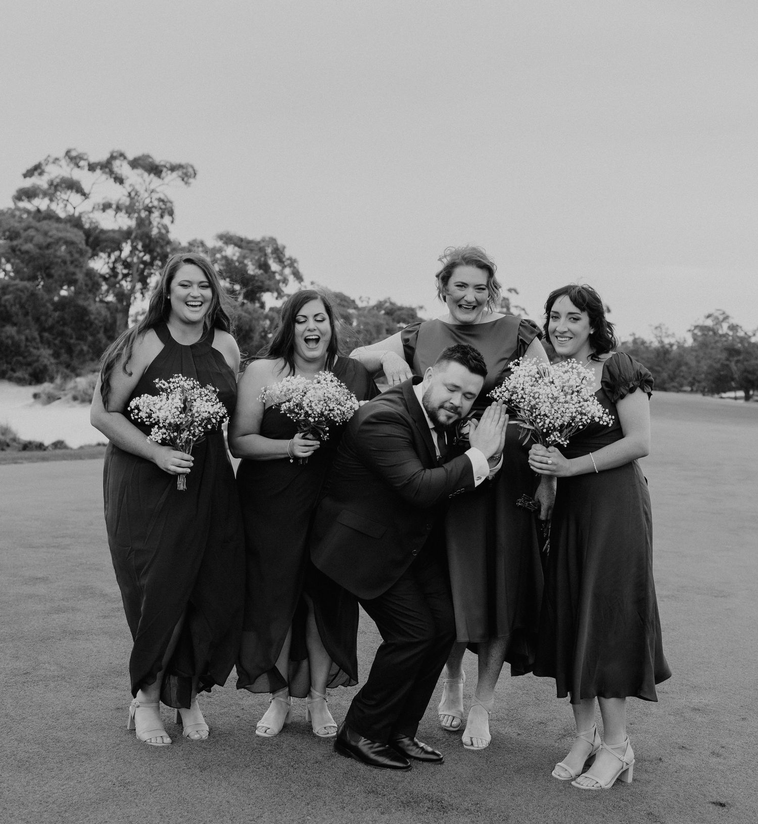 Wedding party poses creatively on ground in black and white photography.