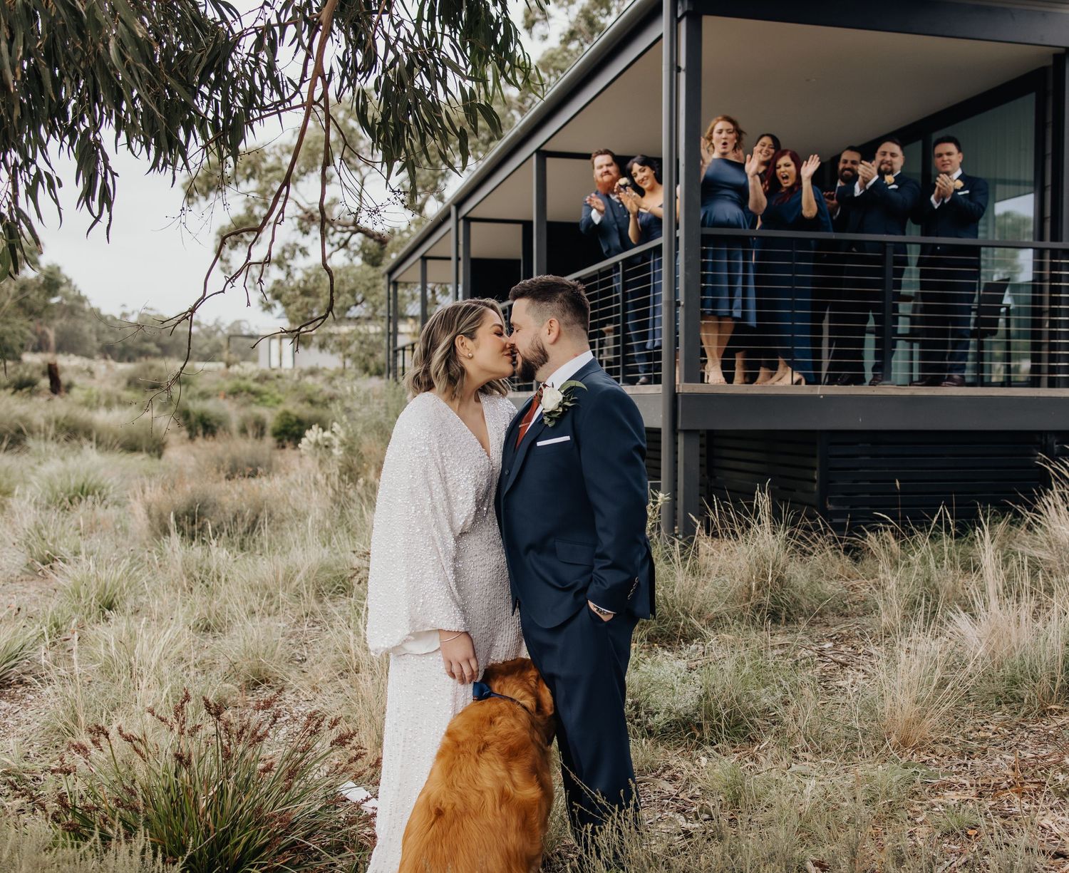 Wedding party poses on modern deck with scenic bush backdrop.