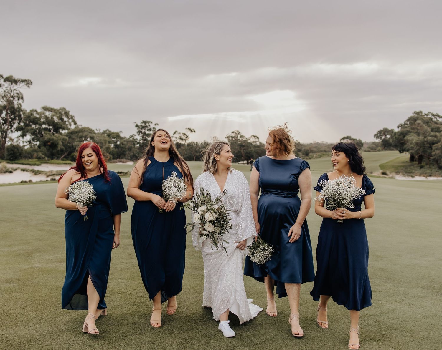 Wedding party walking together across a grassy field during an overcast day.
