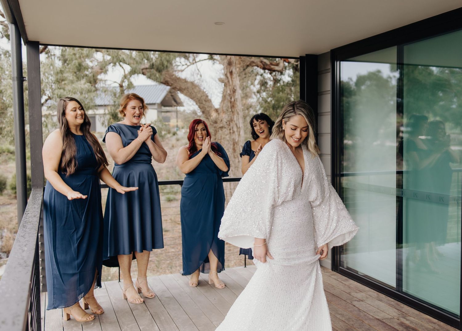 Wedding party in navy and white attire gathered on modern glass-walled patio.