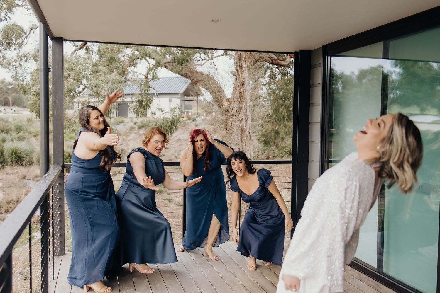 Wedding couple and guests celebrate with joyful jumping poses on modern balcony.