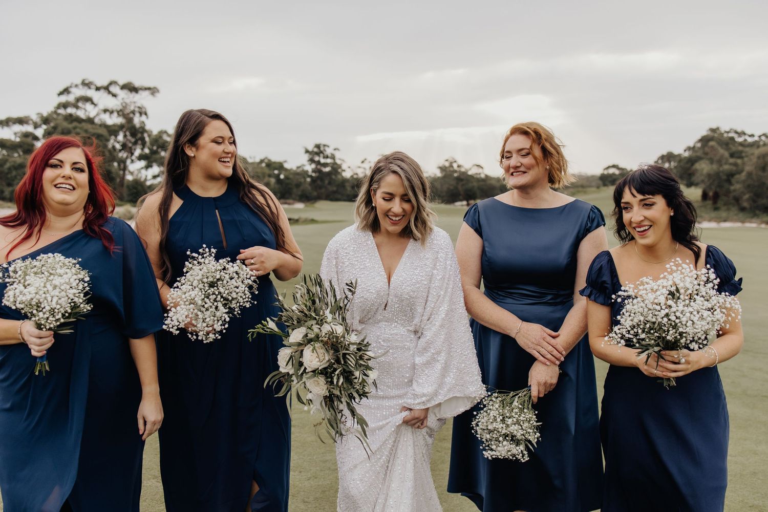 Wedding party poses with white baby's breath bouquets against an overcast sky.