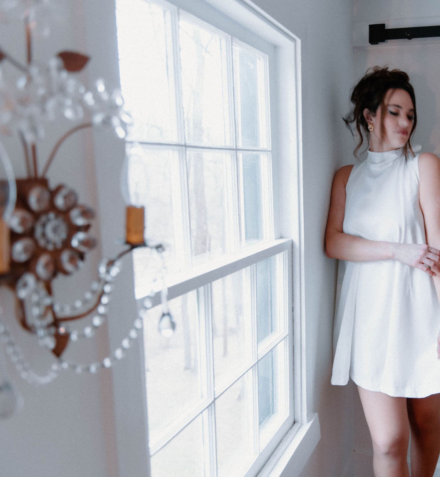 Dreamy white dress photo near a bright window with an elegant chandelier in the foreground.