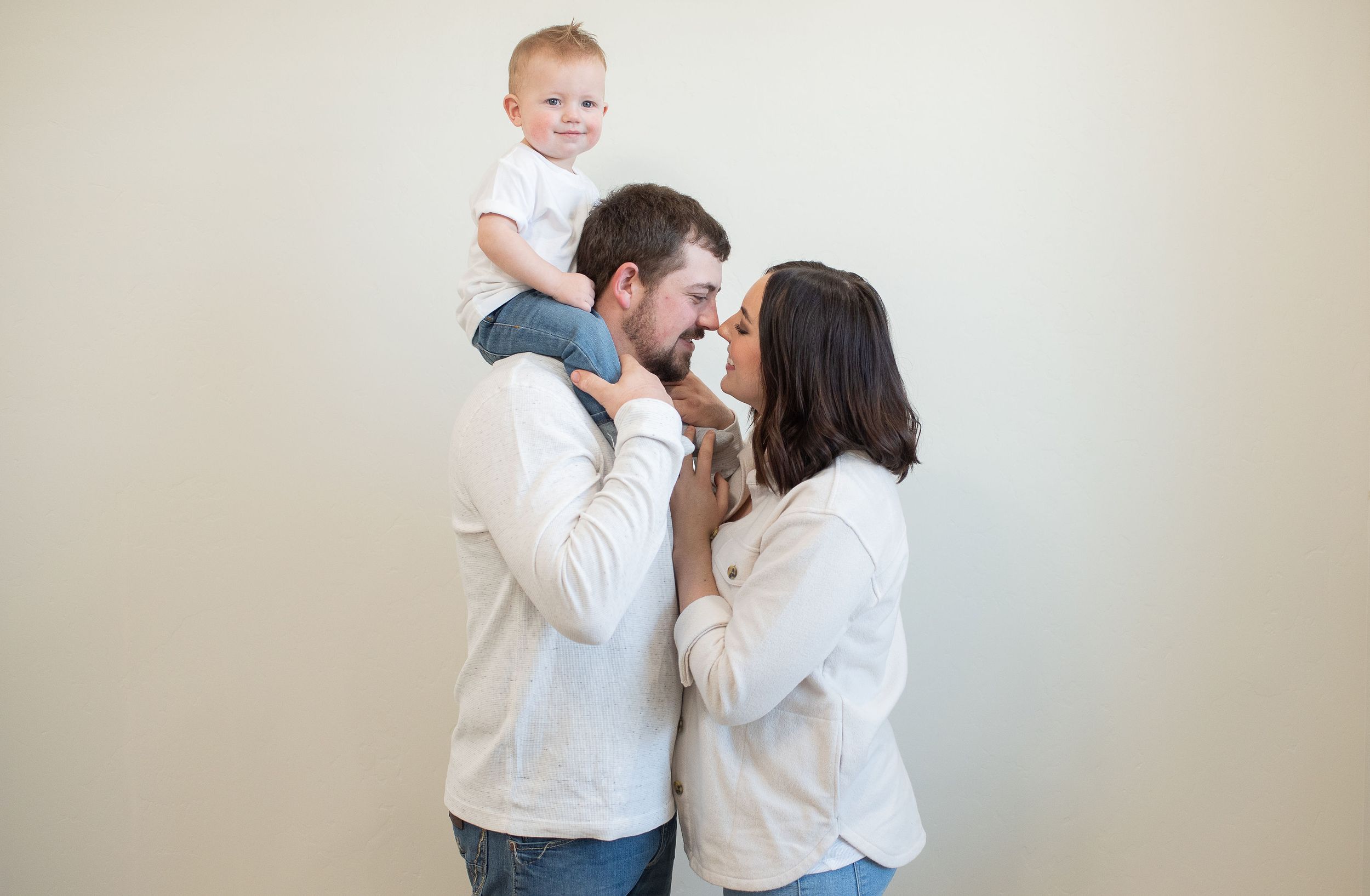 Mom and dad kissing with little boy on dads shoulders smiling