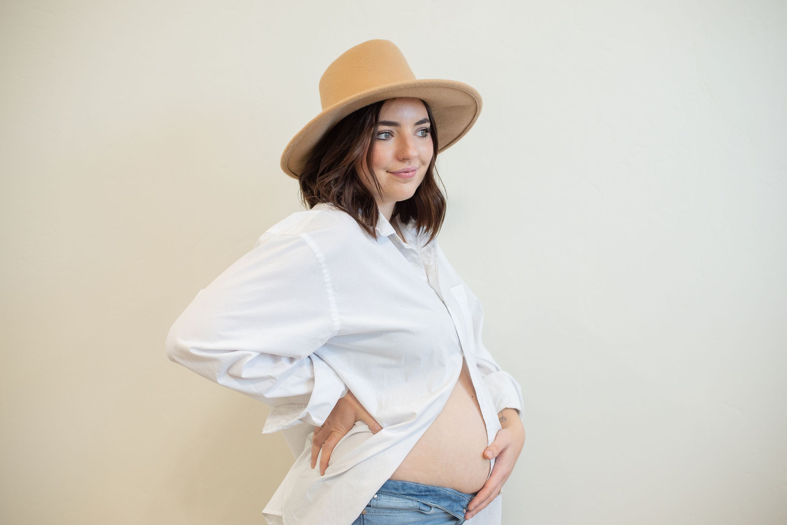 Pregnant mom in white shirt and hat showing belly