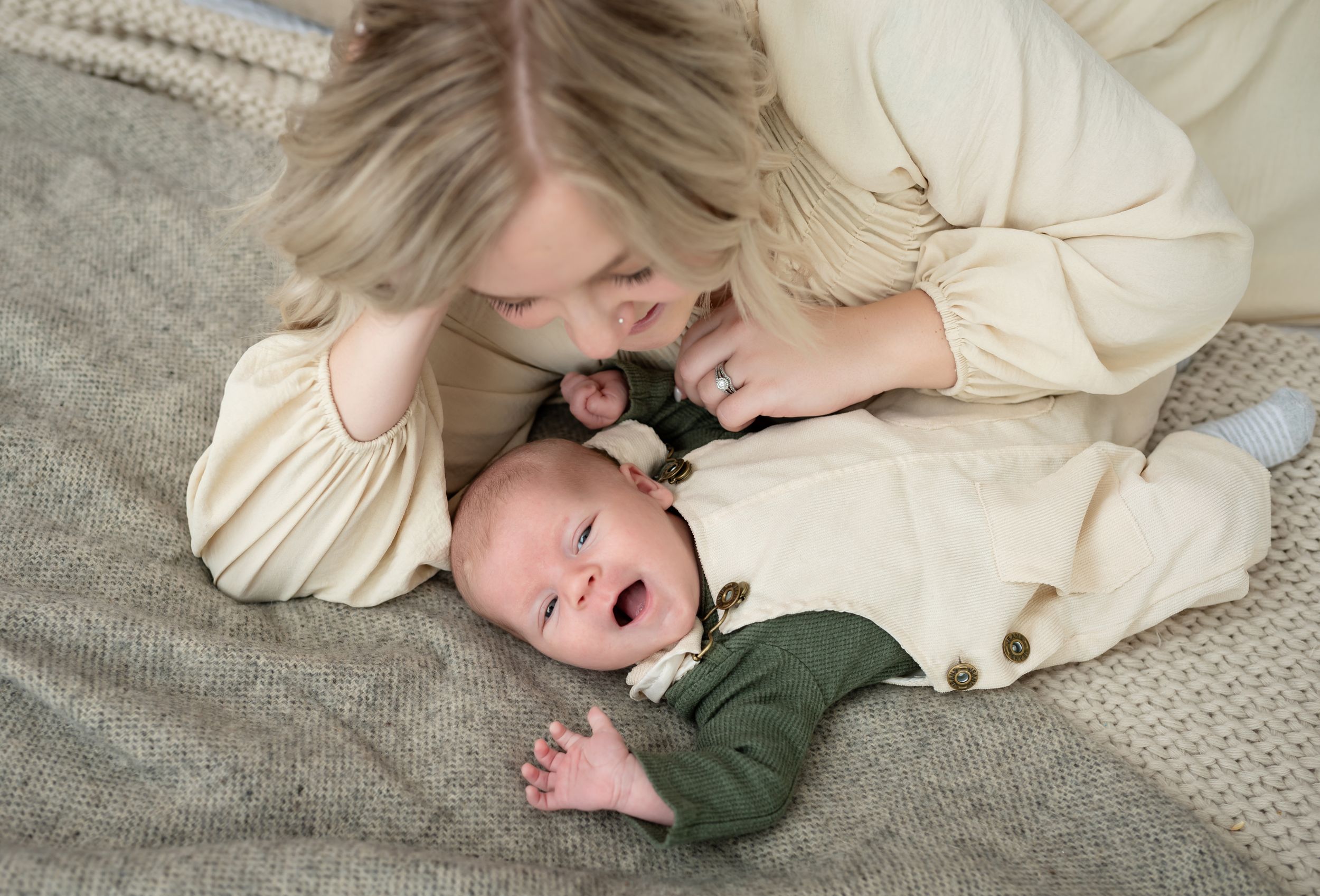 Baby in overalls smiling as mom tickles him