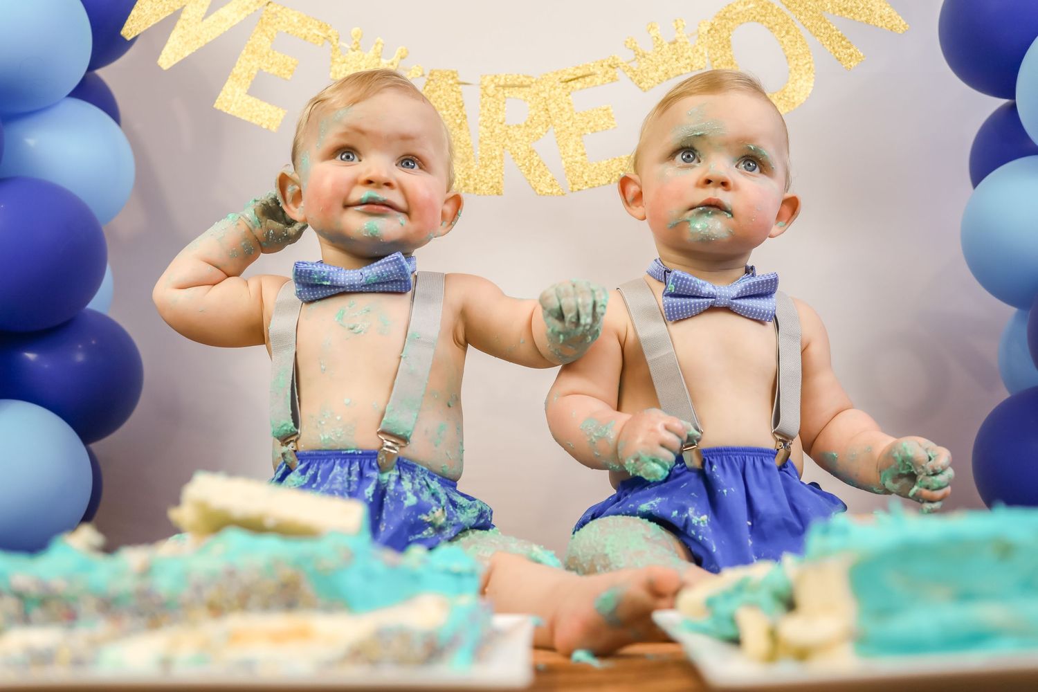 Twin baby boys celebrate their first birthday with a cake smash in blue decorations.