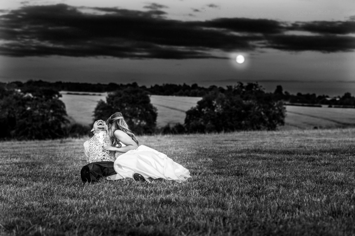 bride and groom sitting on the grass laughing