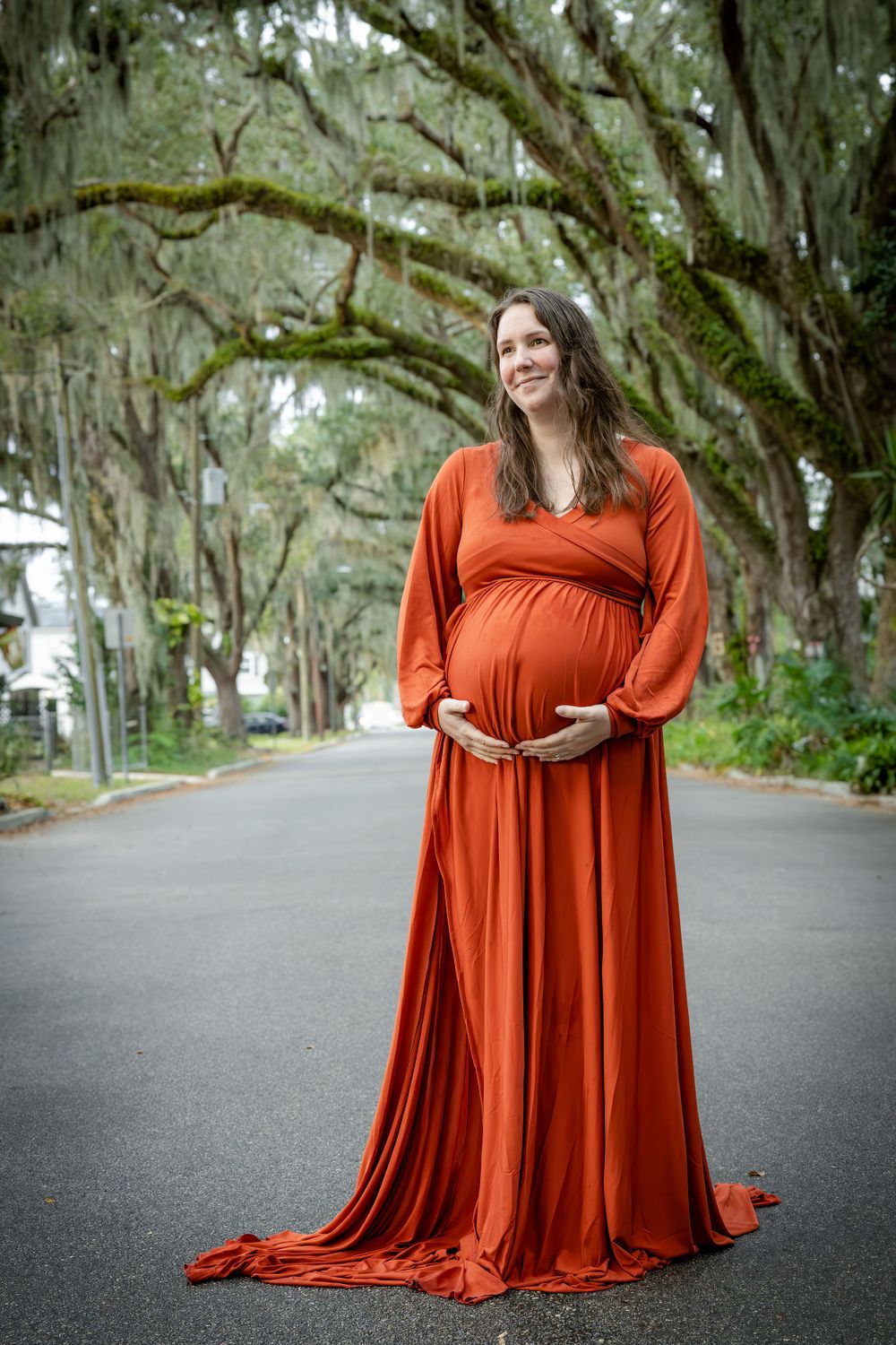 A maternity portrait on a tree-lined street featuring a flowing rust-colored gown.