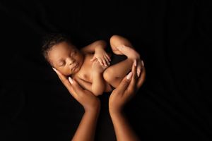 Artistic portrait of newborn baby cradled in hands against black background.