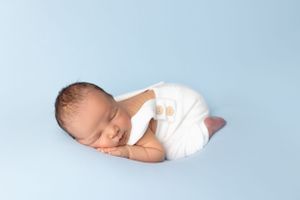 Sleeping newborn in white wrap against soft blue backdrop.