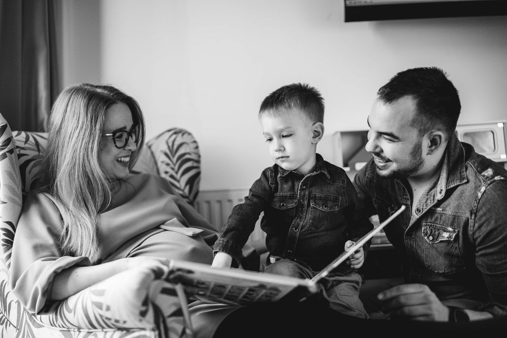A family shares a tender moment reading together on a couch in black and white.