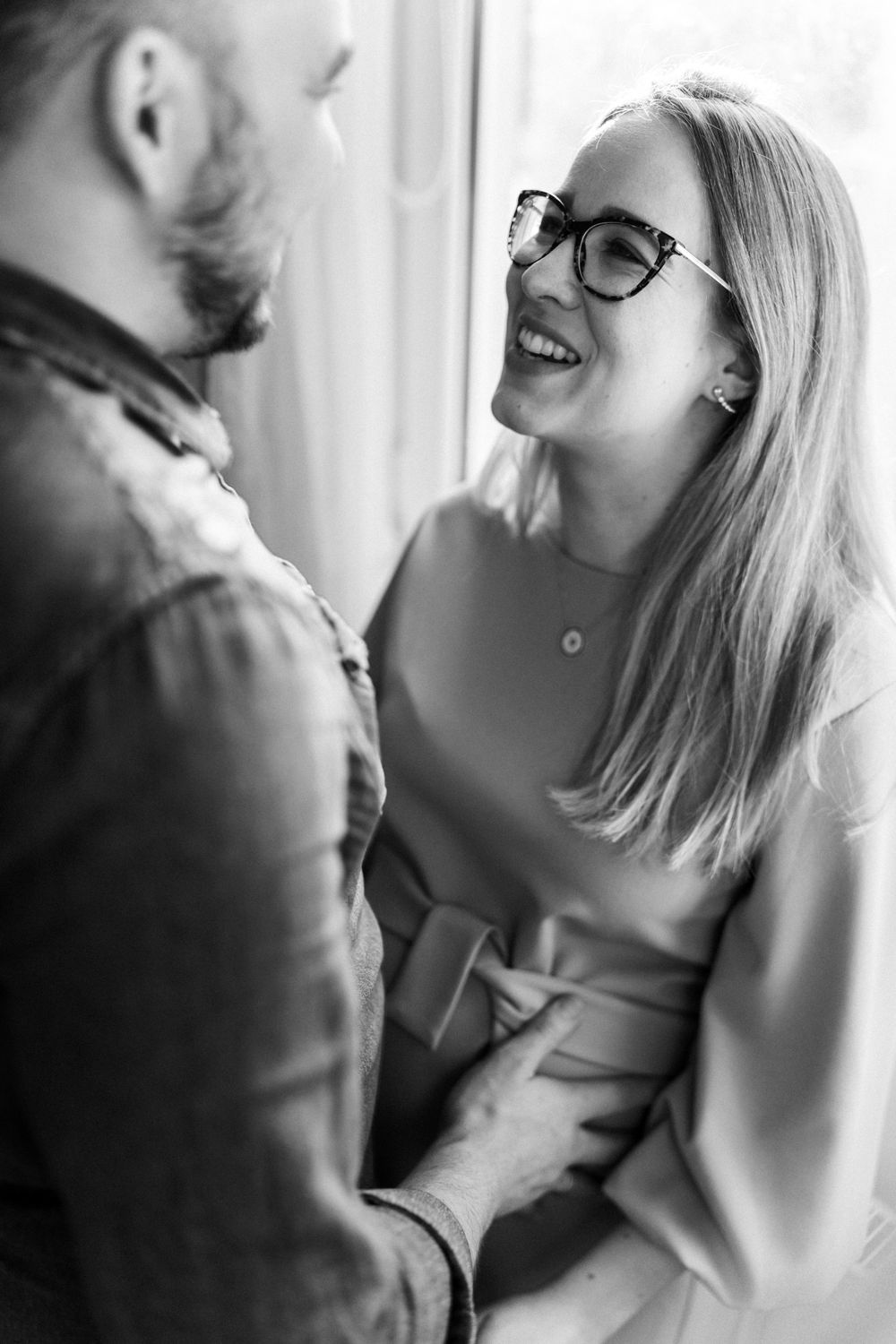 A joyful couple shares an intimate moment near a bright window.